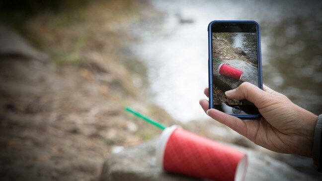 Picture of a camera phone held by hand taking picture of a red cup.
