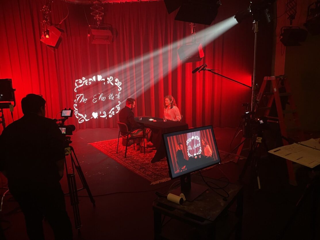 Camera operator films two people on a tv stage that is bathed in red light