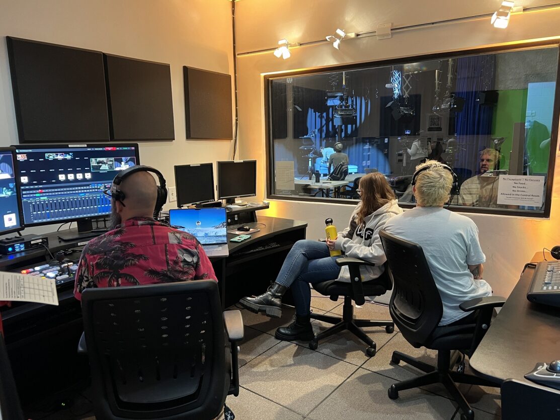 three staff people in a recording booth while filming a tv program