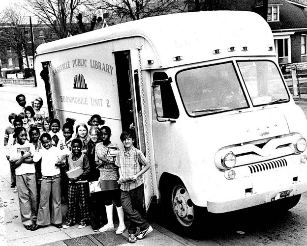 Old bookmobile from the 1950s, a white bus, with children posed in front