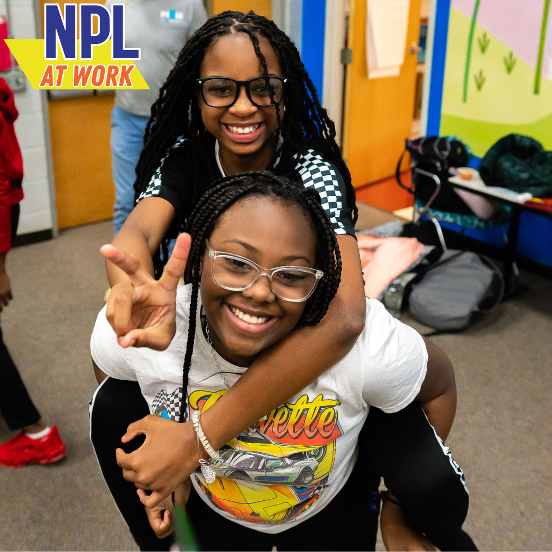 Two women at work at the library giving a peace sign gesture to the camera