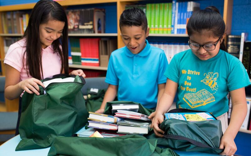 Three middle-school children unpacking books from green shipping bags. 