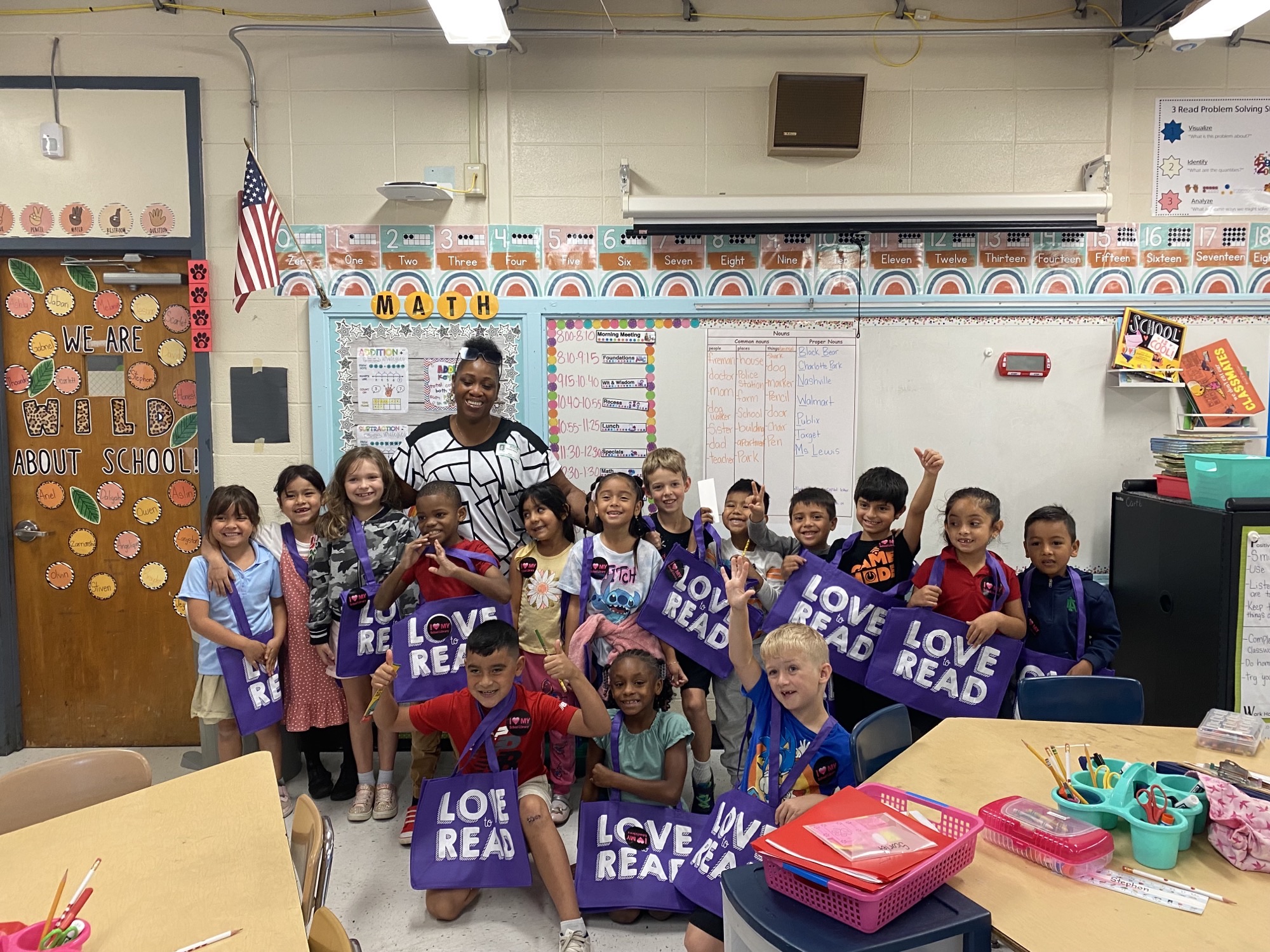 Woman with a black and white shirt stands with a group of children holding purple "Love to Read" bags