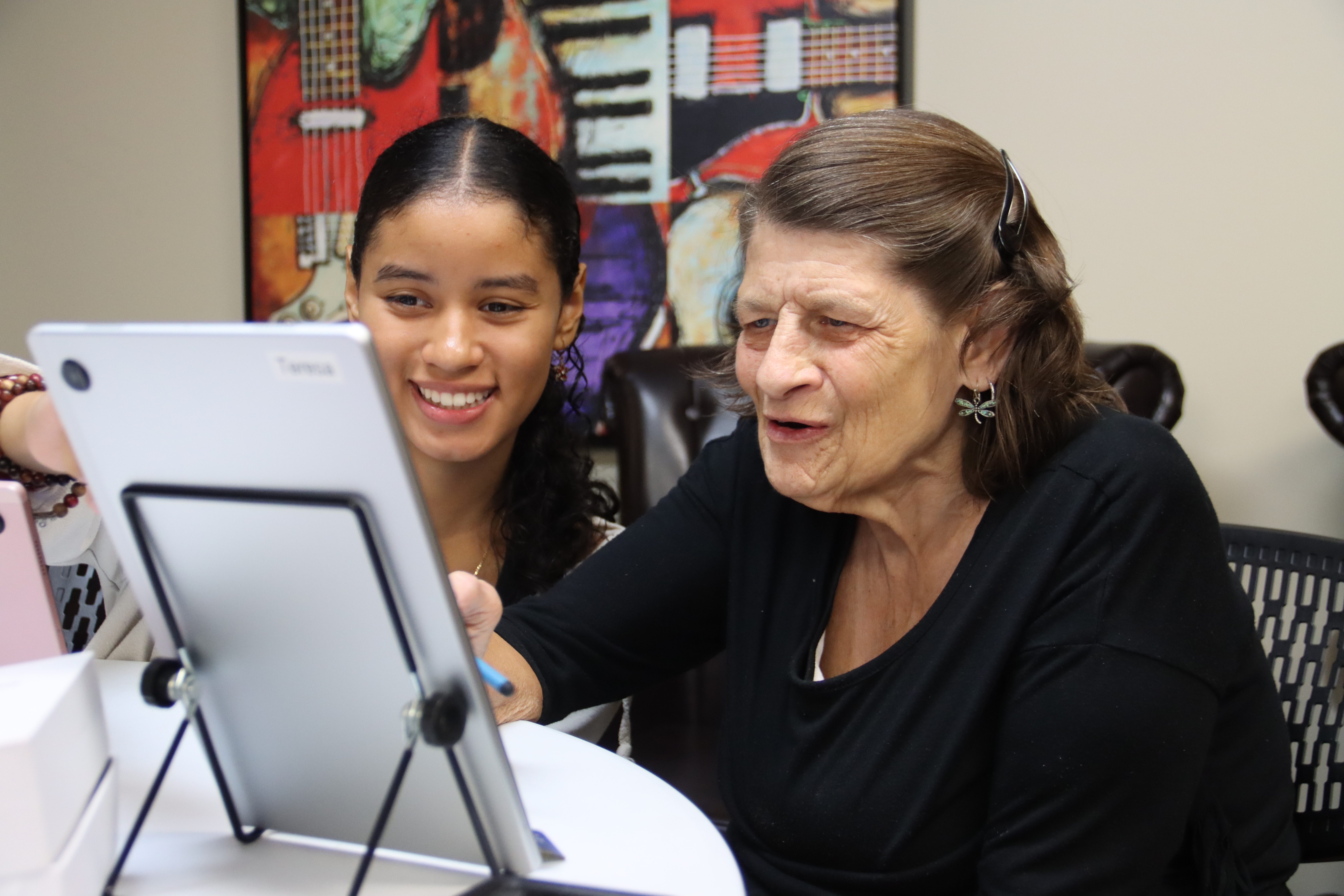 Young girl with dark brown hair helping an older woman with an ipad