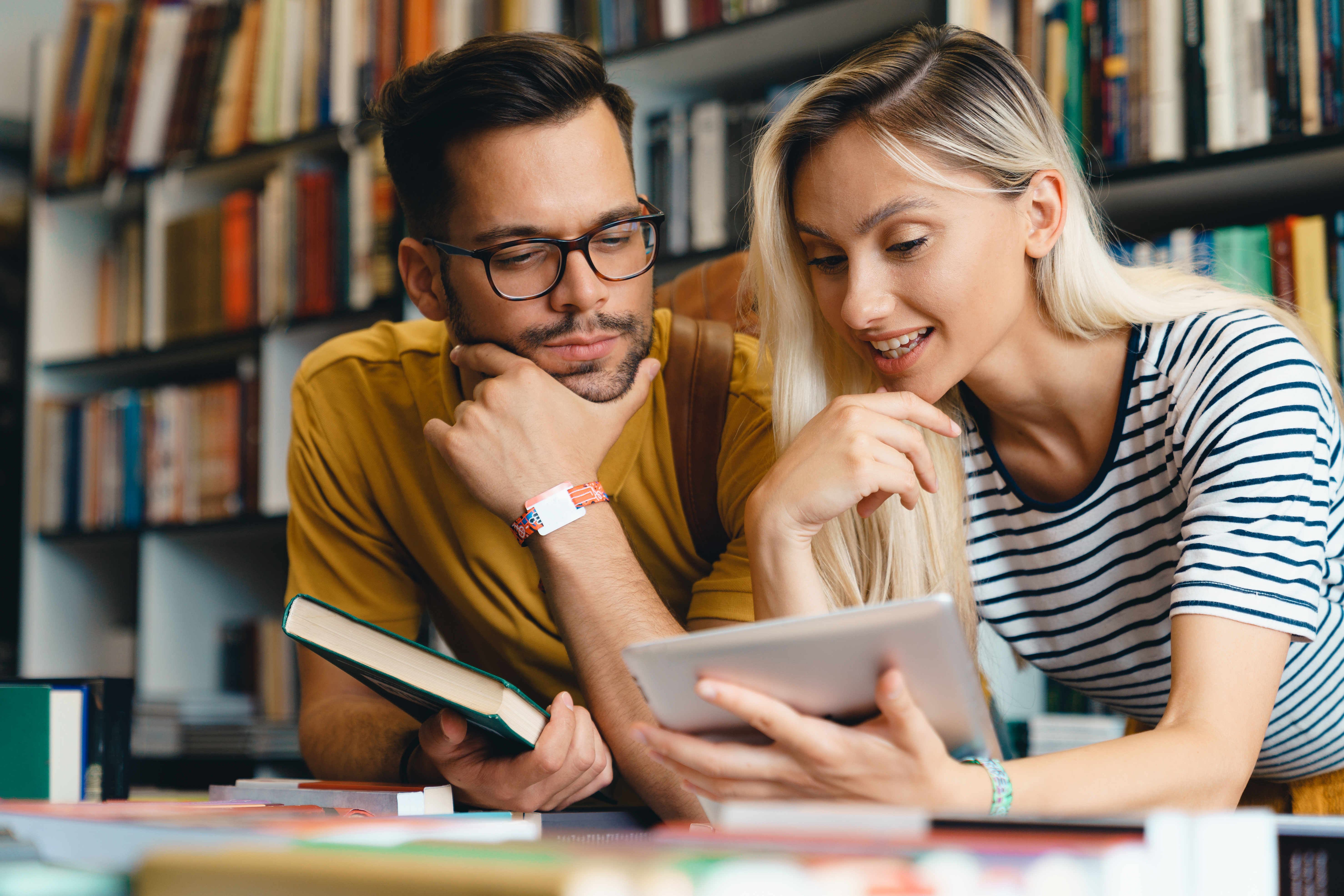 Two adults looking at books and a tablet in a library
