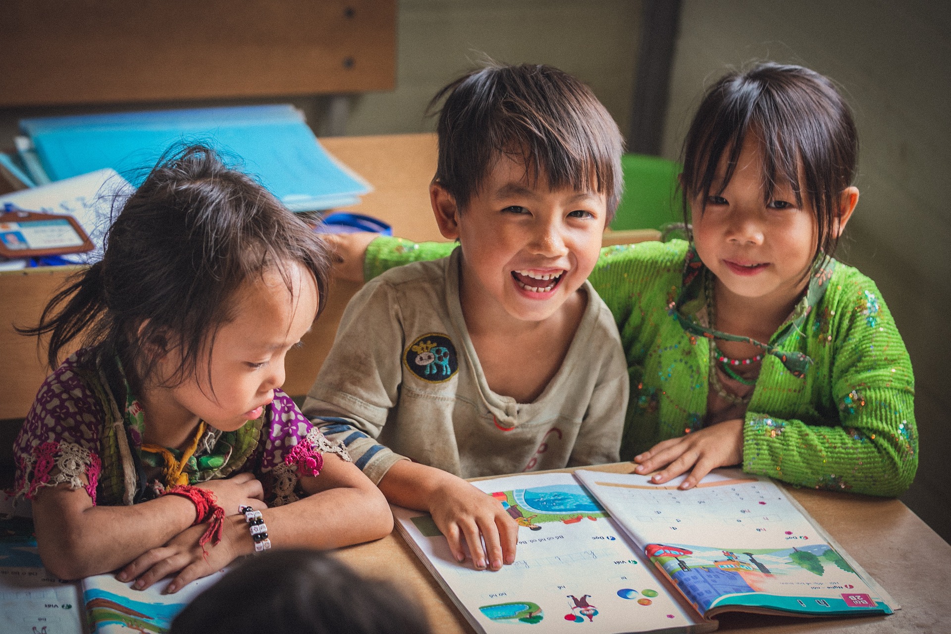 Three young children smiling and laughing while reading a picture book.