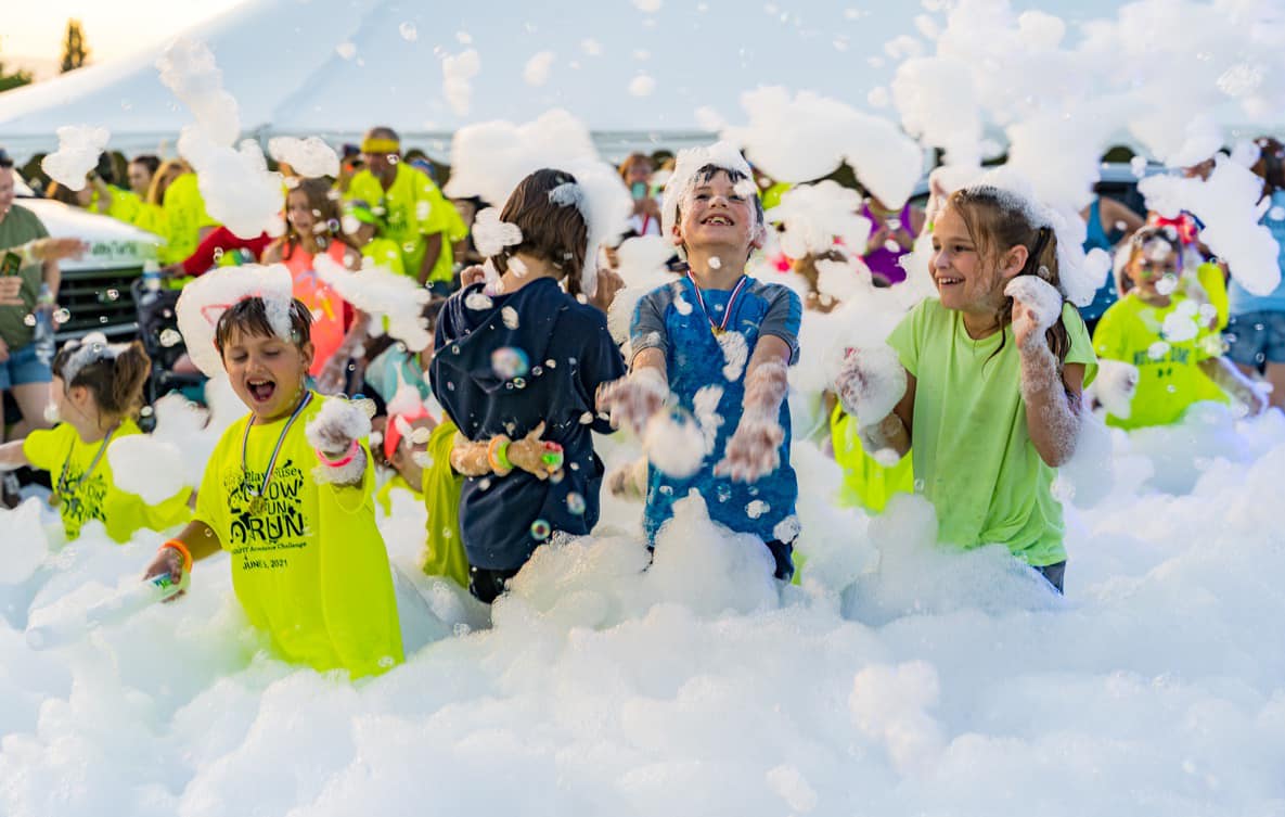 Group of smiling children playing outdoors in a huge pile of foamy soap bubbles.
