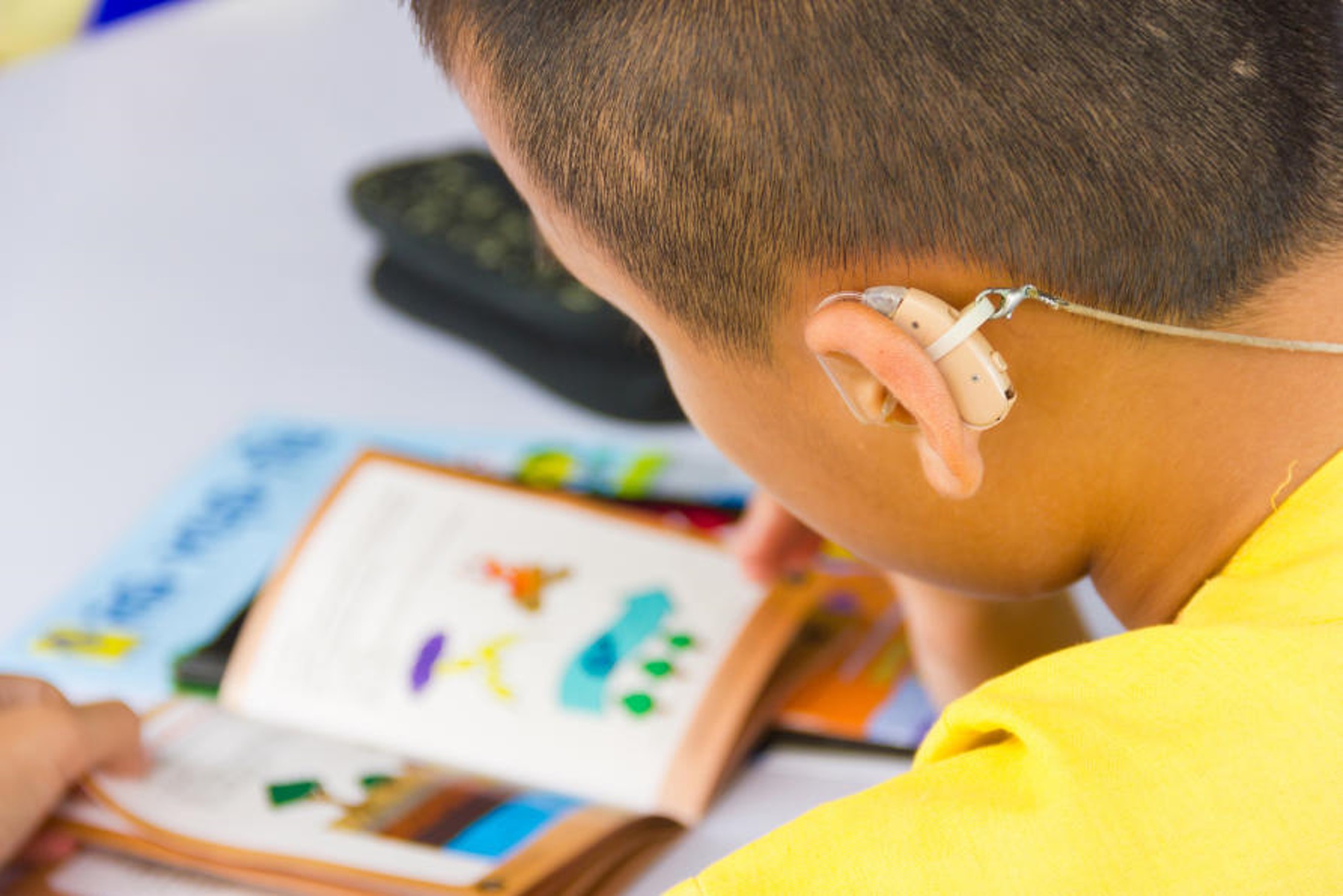 Child wearing a hearing aid and reading a book.