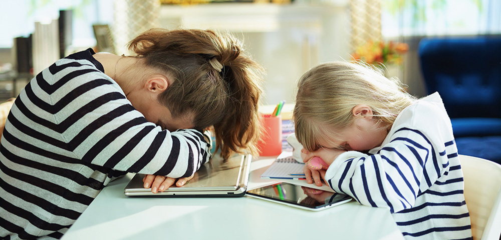 A woman and a child, both wearing black and white stripe shirts, sit at a table with their heads down.
