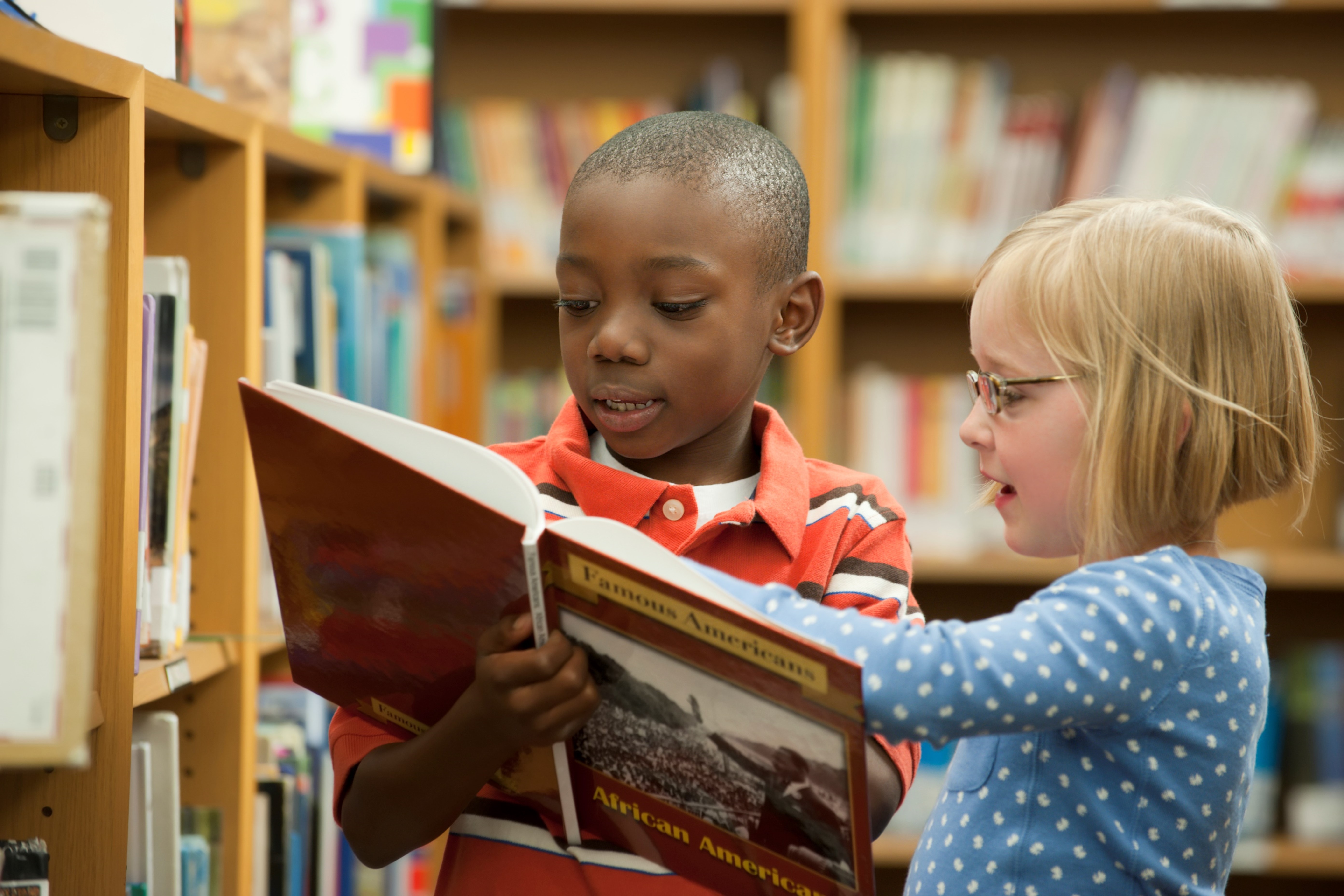 Photography. Two Children inspect a book in library stacks.