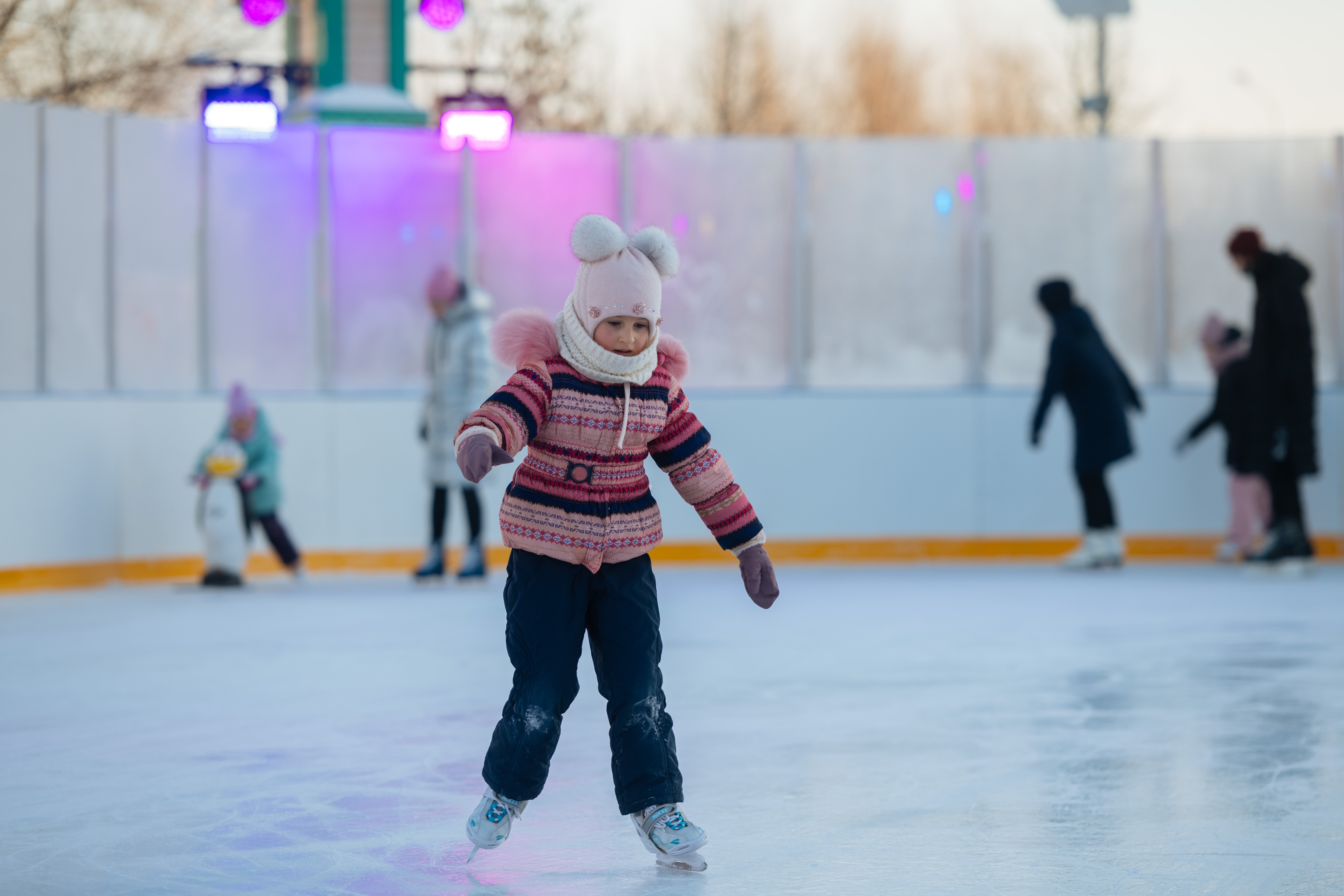 Young girl in a pink hat and pink knit coat ice skates
