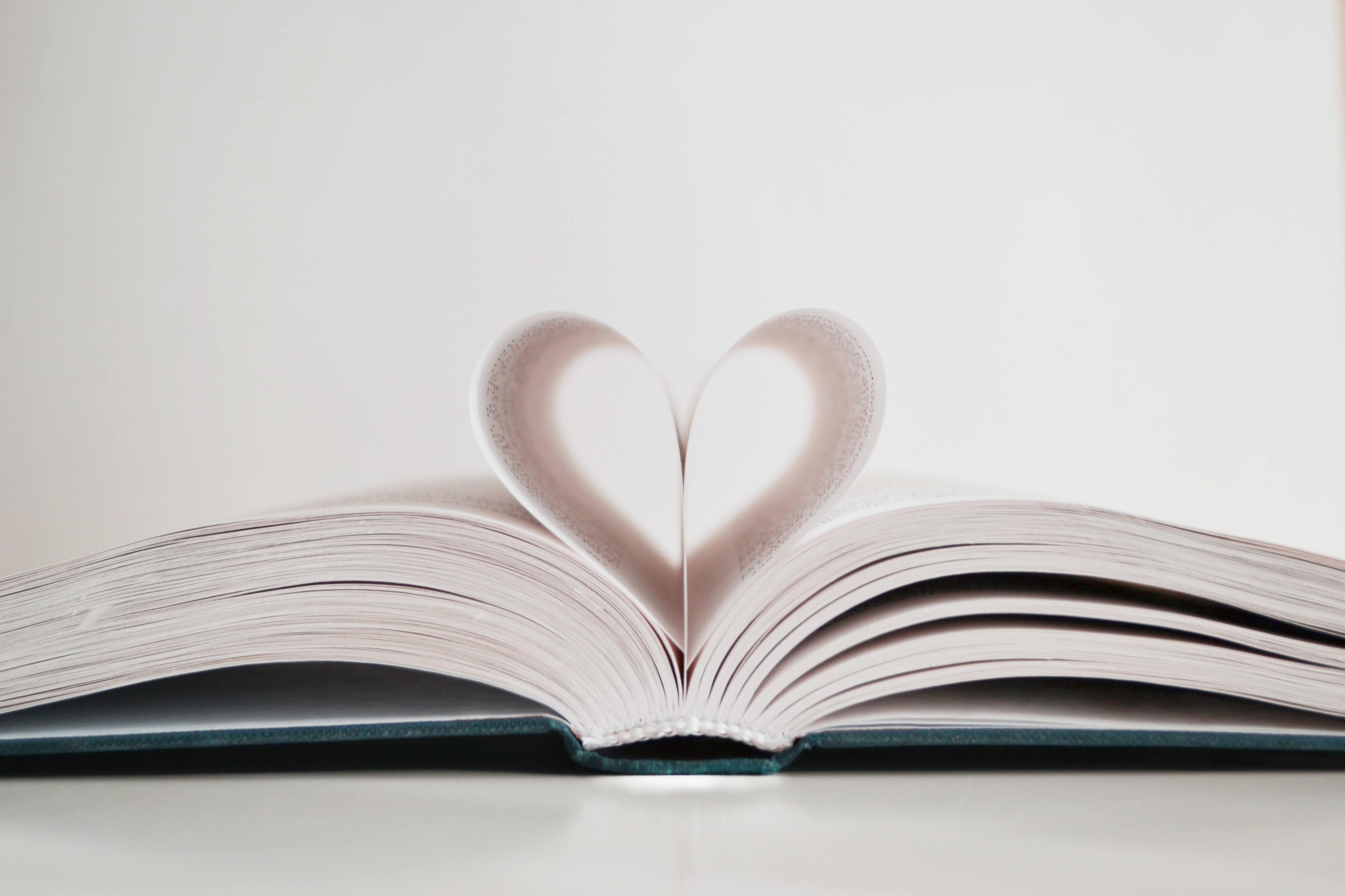 An open book shows two pages curled together to form a heart.