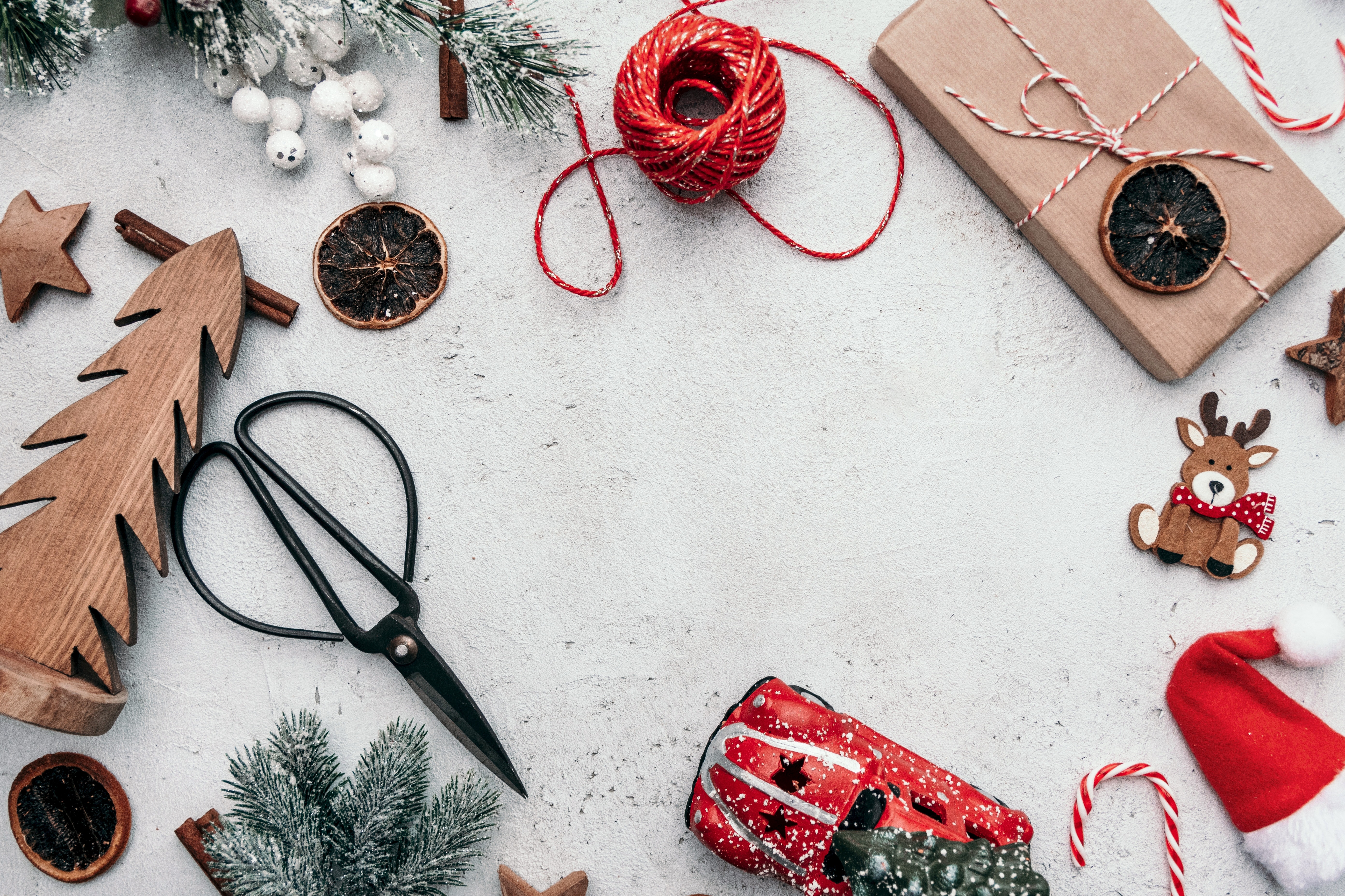 A snowy surface with a wrapped package, black scissors, red twine, a red car, and a pine bough.