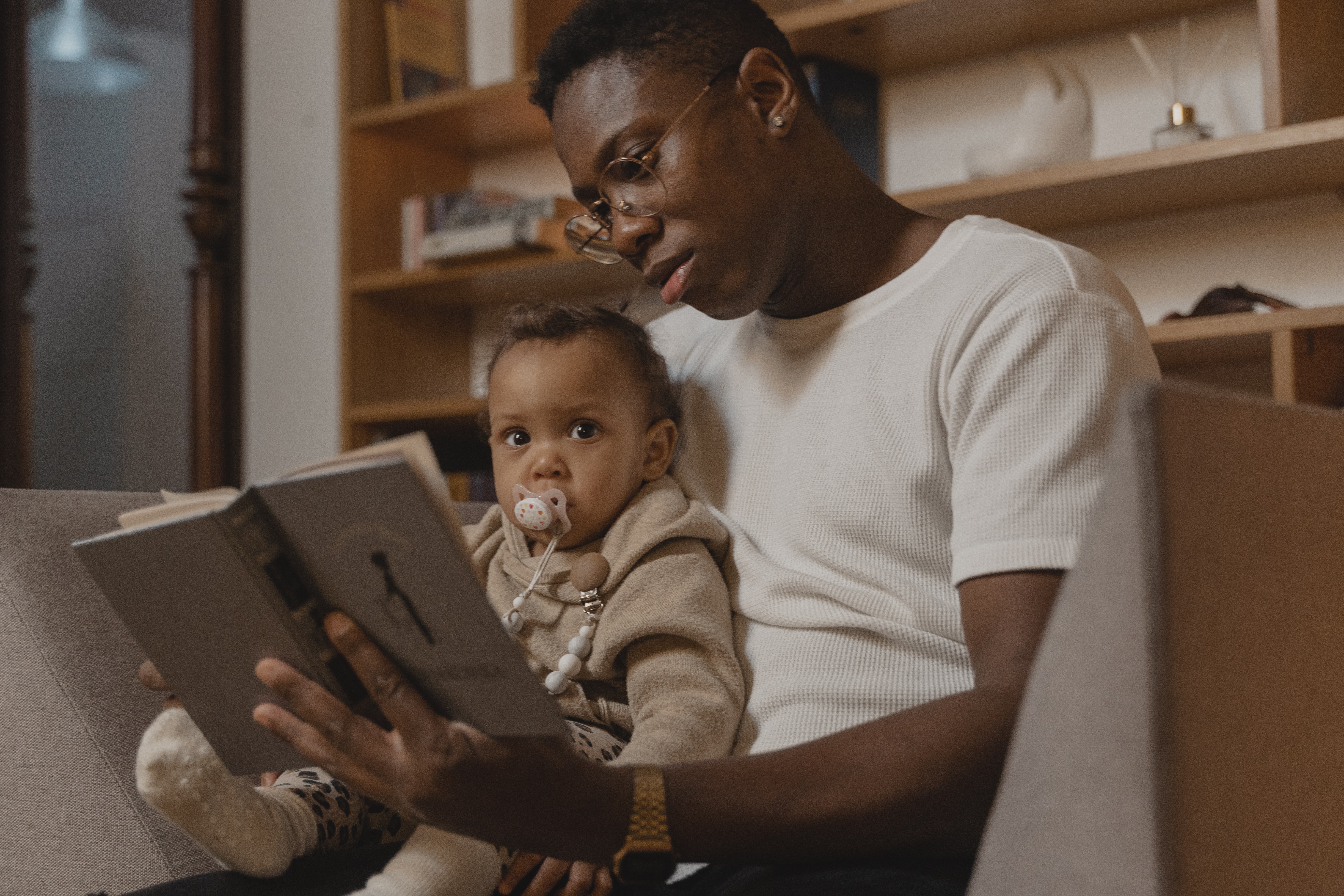 a man holds a baby on his lap while holding a book open in his left hand. 