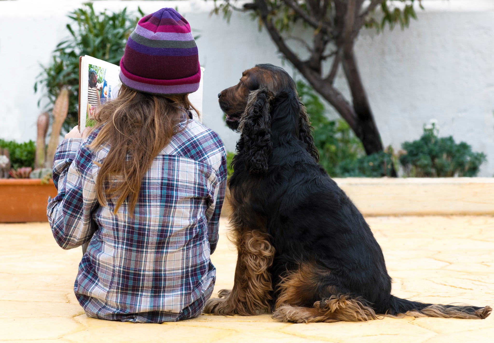 Girl with a purple beanie hat reads to a black dog
