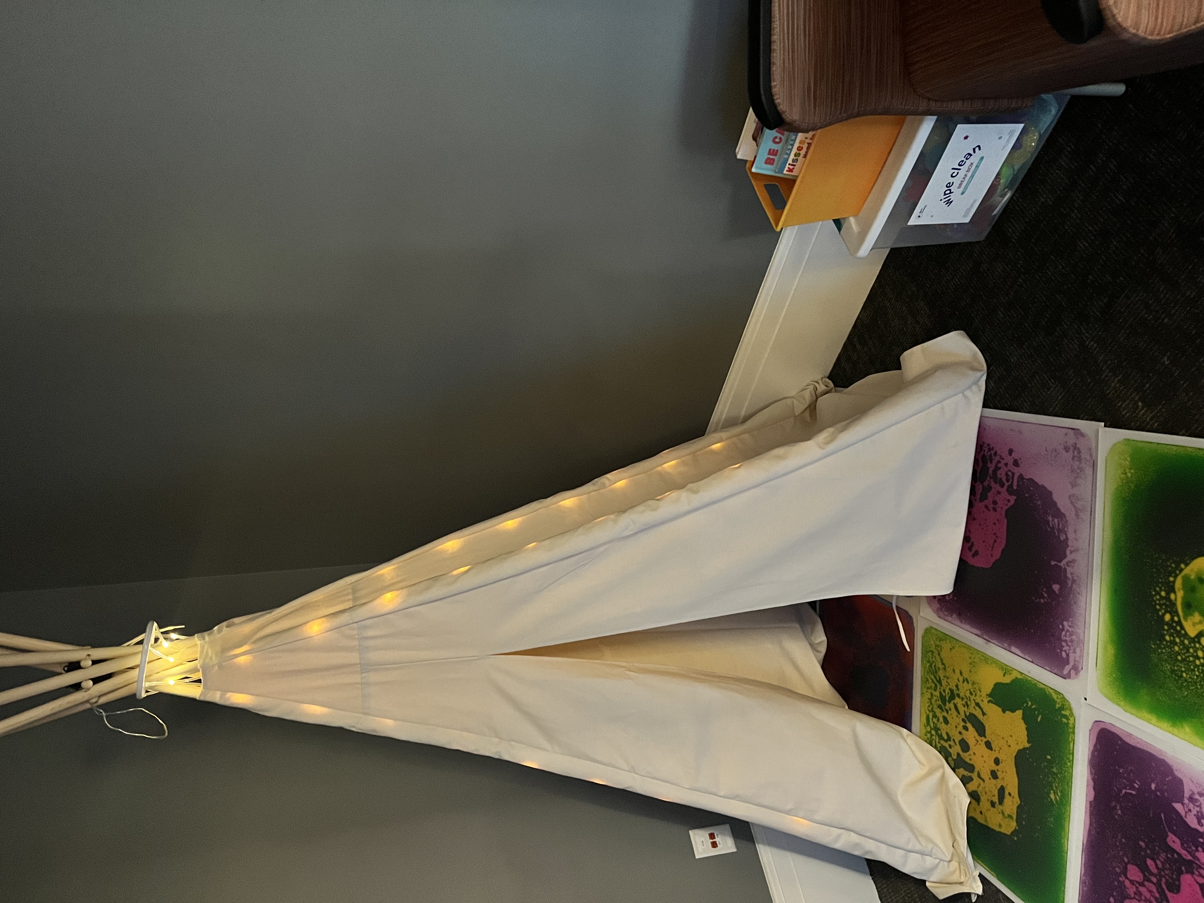 A tee pee sits in the corner of a gray room.