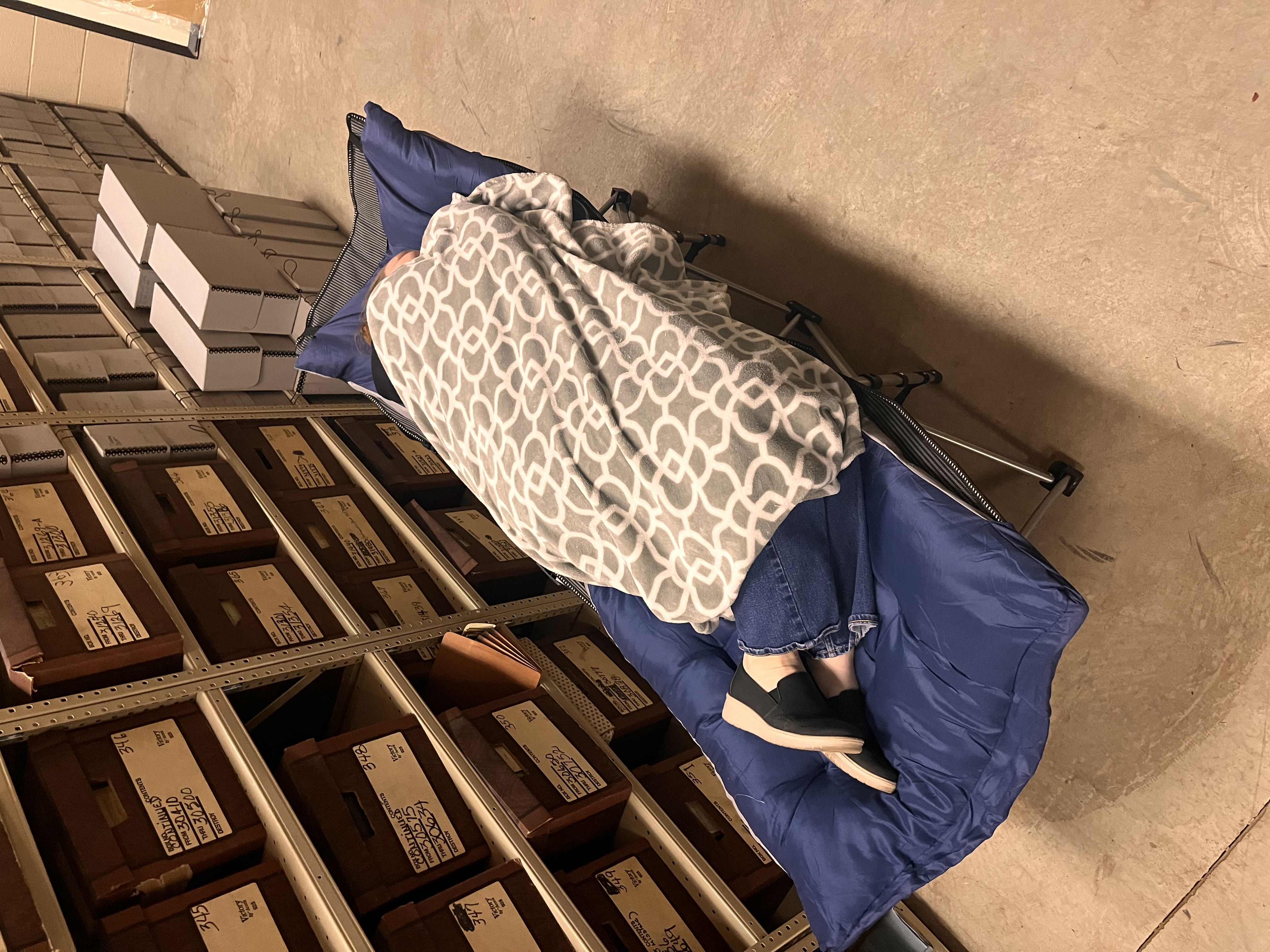 person laying on a blue cot covered in a gray and white blanket
