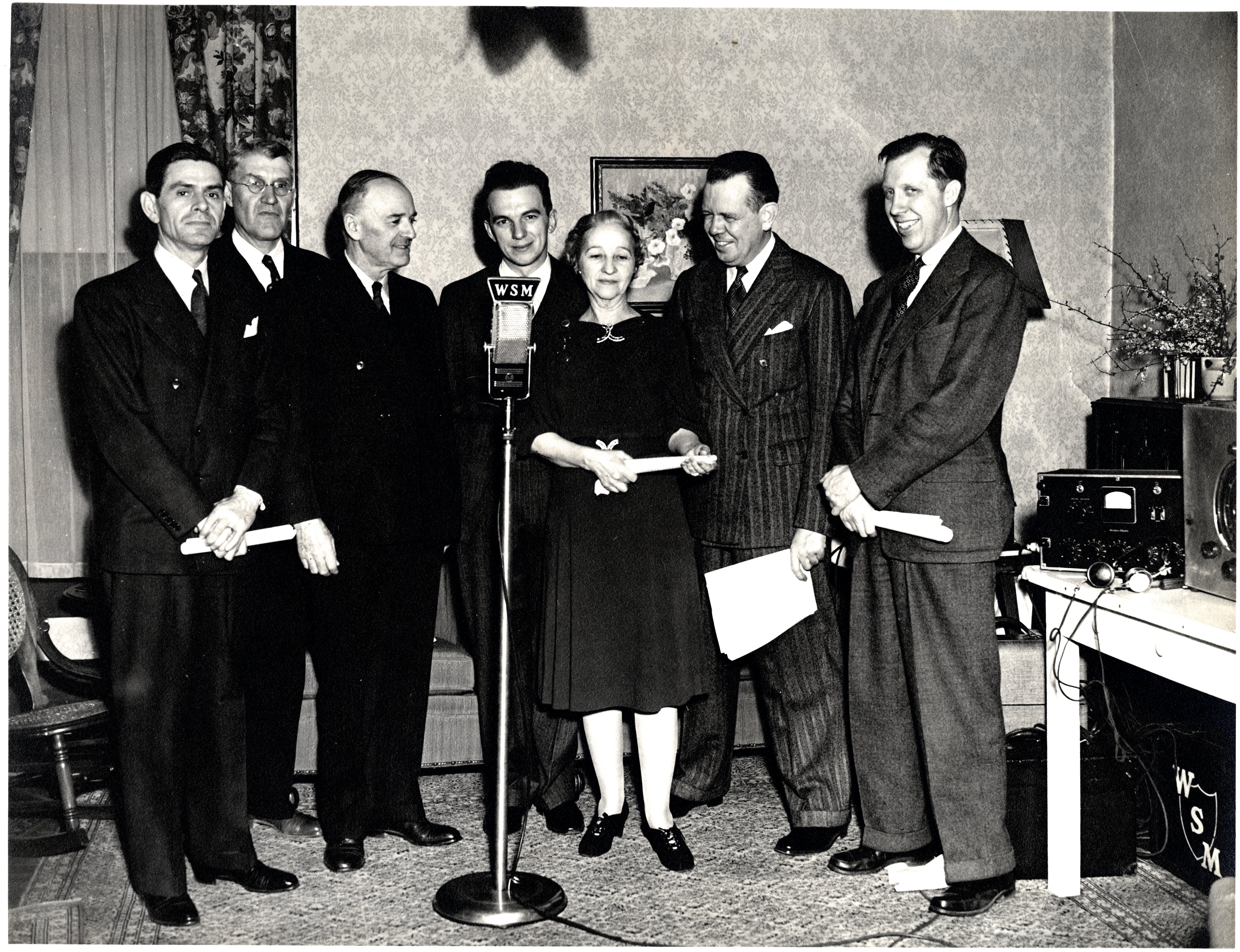 Photo of National Life and WSM staff standing at WSM microphone including Harry Stone, Edwin Craig, and Jack DeWitt