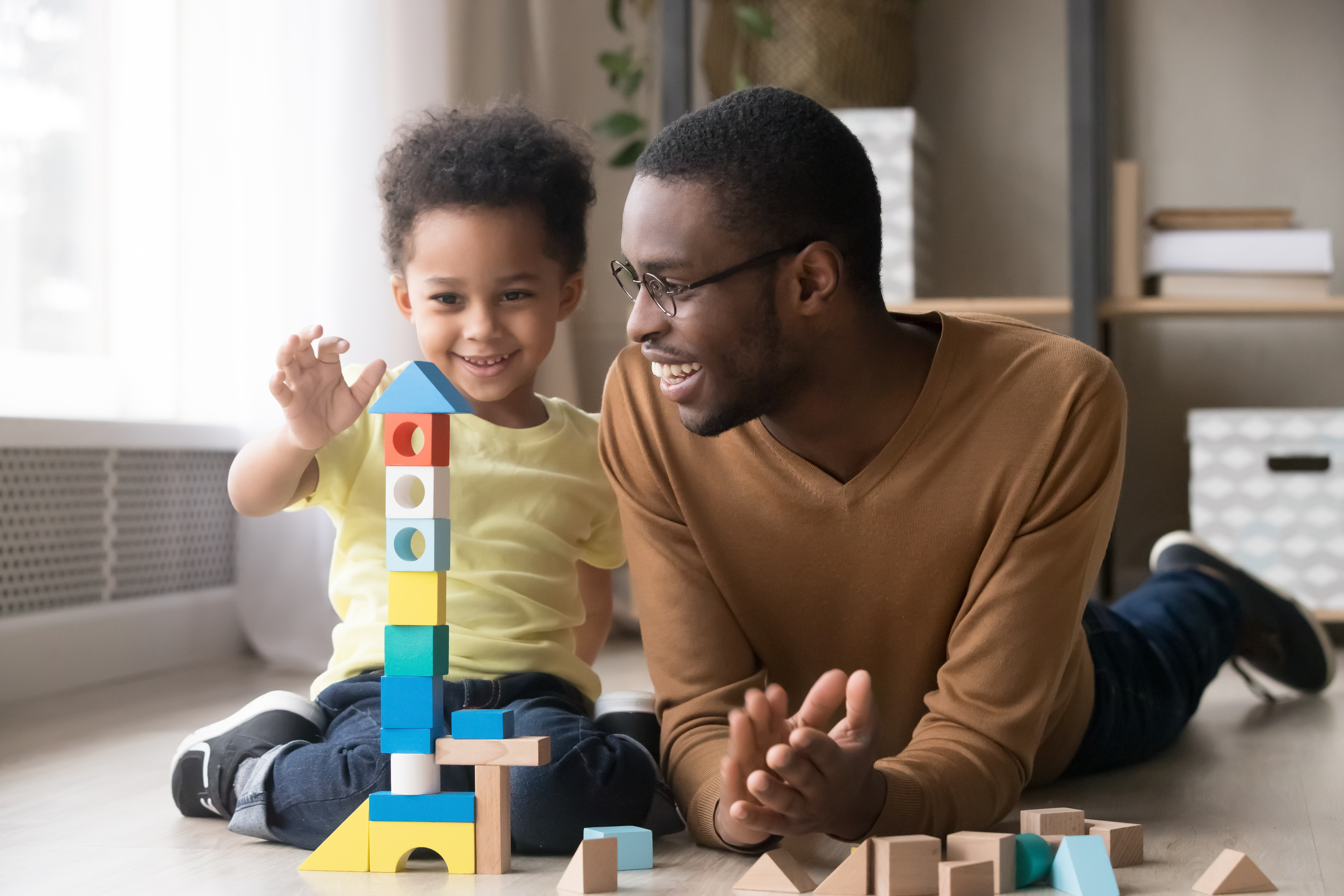 Man and little boy sitting on the floor stacking colorful wood blocks.