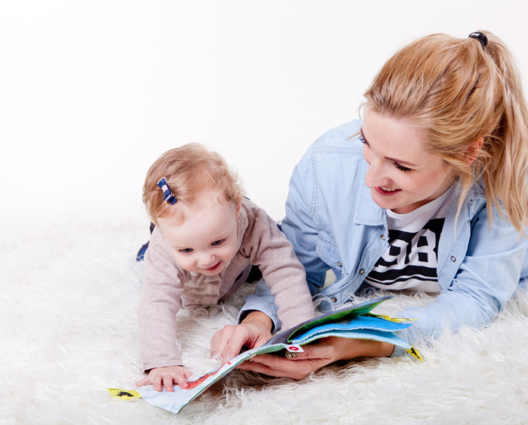 Woman and baby on fur blanket looking at a book.