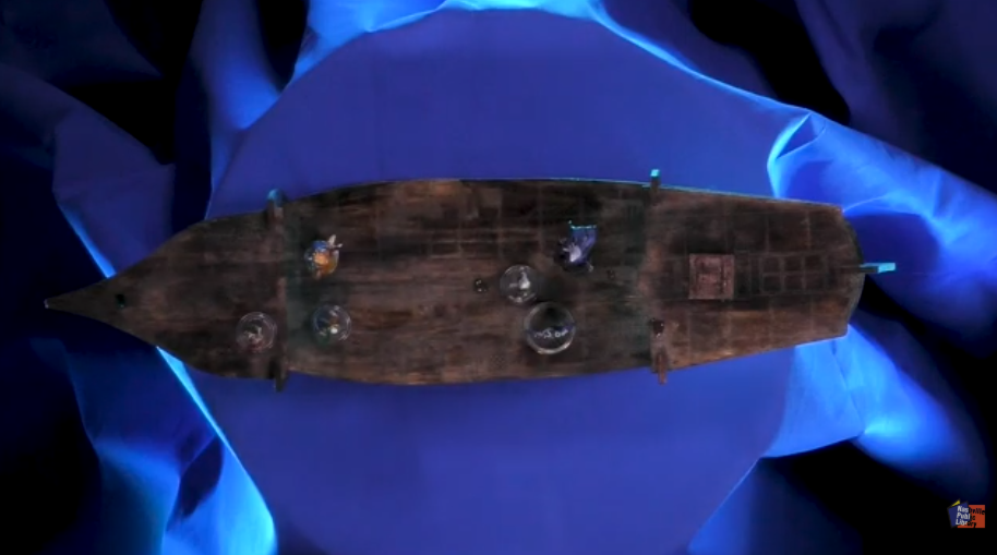 boat with six miniatures on top. Sitting on blue cloth. 