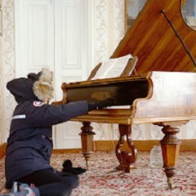 Person in a parka sits on the floor playing a large piano.