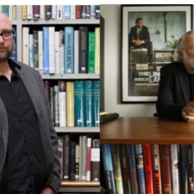 Two men standing in front of book cases.