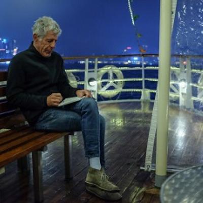 Anthony Bourdain sits on a bench on a ferry.
