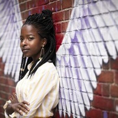 Woman standing against a brick wall with a mural depicting angel wings.