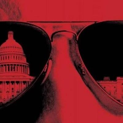 Red and black image that is a close up of someone's head, where sunglasses cover the eye area, and the U. S. Capital is reflected in the lenses.