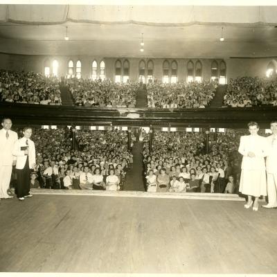 View of the Ryman Auditorium with people on stage and the crowd facing the camera