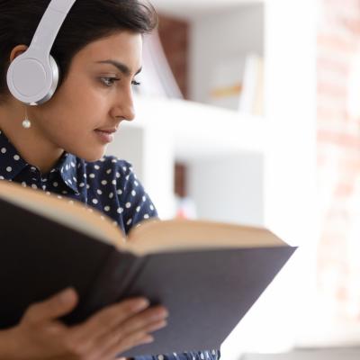 Woman reading a print book while wearing headphones