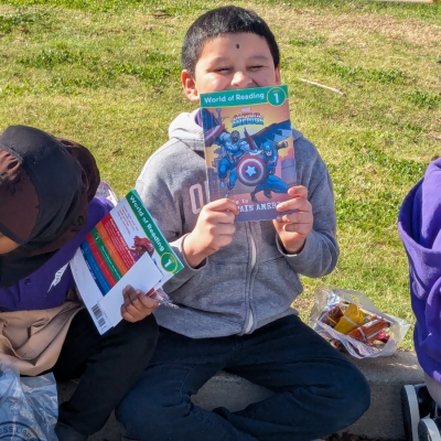 Children sitting on a lawn holding books.