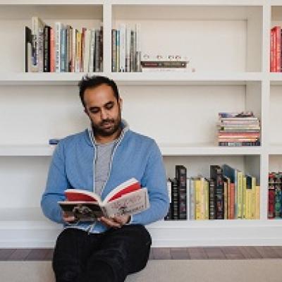 Man sitting in front of a book case reading a book.