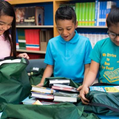Three schoolchildren taking books out of green bags.