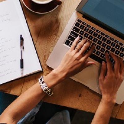 Overhead shot of a woman typing on a laptop surrounded by books and papers.