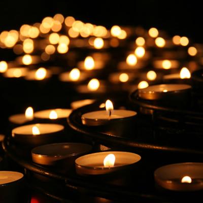 Dozens of lit votive candles against a black background.