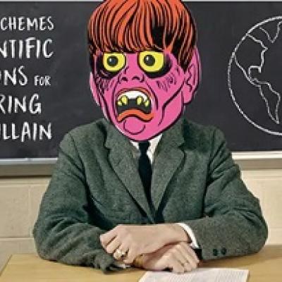 Man in a green suit jacket sits at a desk in front of a chalkboard, but instead of a human head, there is a pink monster illustrated head.