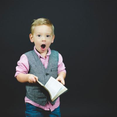 Little boy in pink button down and grey waistcoat with surprised expression. 