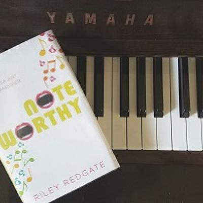 Book called Noteworthy placed on a piano keyboard.