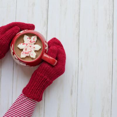 Overhead view of arms with red mittens holding hot chocolate.