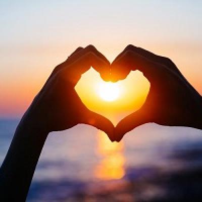 Hands making a heart with a sunset in the background.