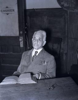 Elderly man in suit and tie sitting at a table.