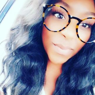 Black woman with wavy black hair and wearing large round tortoiseshell glasses.