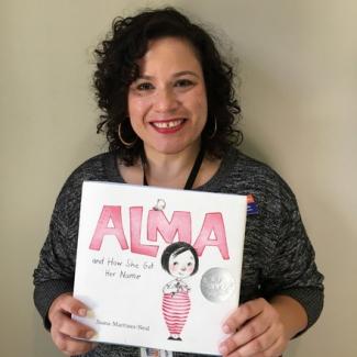 Photograph. Klem-Marí holds Childrens picture book, _Alma_.