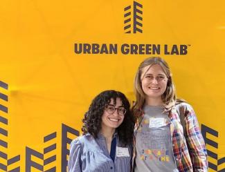 Two women pose in front of the Urban Green Lab logo