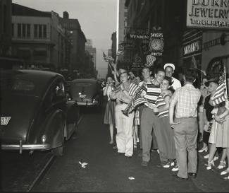 Men and women stand on the side of a road in downtown Nashville holding American flags