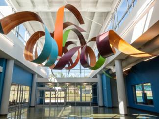 From the Four Corners is a multi-colored sculpture made of four different wood species and brightly colored plastic laminate are shaped into curling, spiraling strips and intertwined into a loose knot.